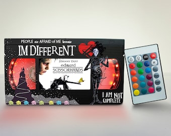 May include: A black VHS tape with a red light around the edges. The tape has a picture of Johnny Depp as Edward Scissorhands on the front. The text on the tape reads "People are afraid of me because I'm different." and "I am not complete".