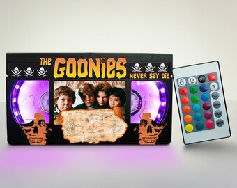 May include: A black VHS tape-style light with a picture of the Goonies characters and a treasure map. The light has a skull design on each side and a remote control with color changing LED lights.