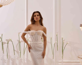 May include: A white off-the-shoulder wedding dress with a fitted bodice and a flowing skirt. The dress is embellished with delicate beading and lace.