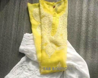 Puede incluir: Una kurta amarilla bordada con una falda bordada blanca. La kurta tiene un escote redondo y un cierre de botón. La falda tiene una silueta acampanada y un ribete de encaje.