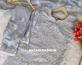 May include: A gray embroidered dress with a matching dupatta and pants. The dress has a V-neckline and is decorated with white floral embroidery. The text "SADAGI FASHION" is visible on the dress.