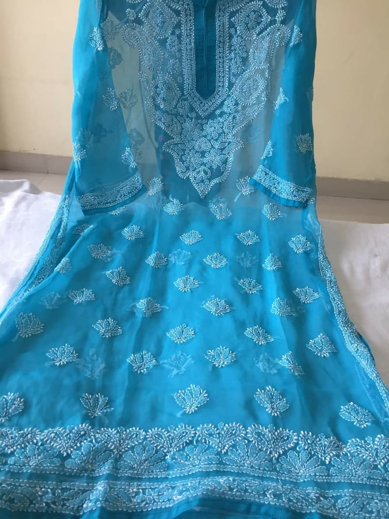 May include: A turquoise blue sheer tunic with white embroidery. The embroidery features floral and paisley designs. The tunic has a round neckline and three-quarter sleeves.