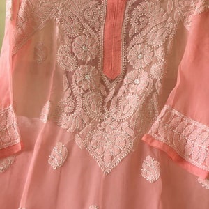 May include: A peach-colored sheer tunic with white embroidery. The embroidery features floral and paisley designs.