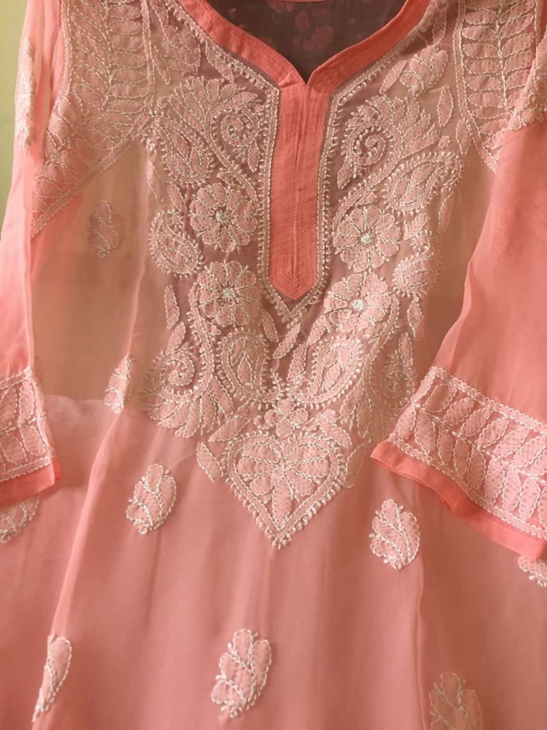 May include: A peach-colored sheer tunic with white embroidery. The embroidery features floral and paisley designs.