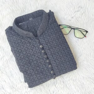 Pode incluir: Uma kurta preta estampada com gola mandarim e fecho de bot&otilde;es. A kurta est&aacute; dobrada e colocada sobre uma superf&iacute;cie branca e felpuda.