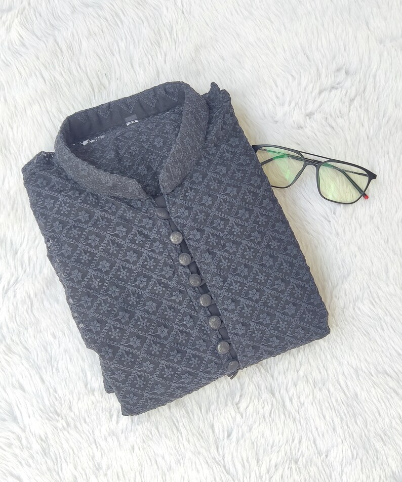 Pode incluir: Uma kurta preta estampada com gola mandarim e fecho de bot&otilde;es. A kurta est&aacute; dobrada e colocada sobre uma superf&iacute;cie branca e felpuda.