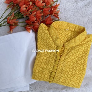 Pode incluir: Uma kurta amarela bordada com gola branca e fecho de bot&otilde;es. A kurta &eacute; feita de um tecido leve e tem um delicado padr&atilde;o floral. O texto "SADAGI FASHION" &eacute; vis&iacute;vel na kurta.
