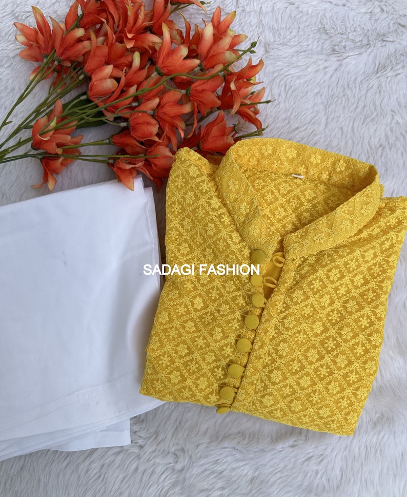 Pode incluir: Uma kurta amarela bordada com gola branca e fecho de bot&otilde;es. A kurta &eacute; feita de um tecido leve e tem um delicado padr&atilde;o floral. O texto "SADAGI FASHION" &eacute; vis&iacute;vel na kurta.