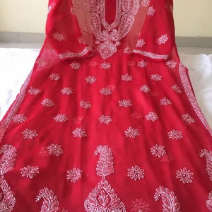 May include: A red sheer tunic with white embroidery. The embroidery features floral and paisley designs.