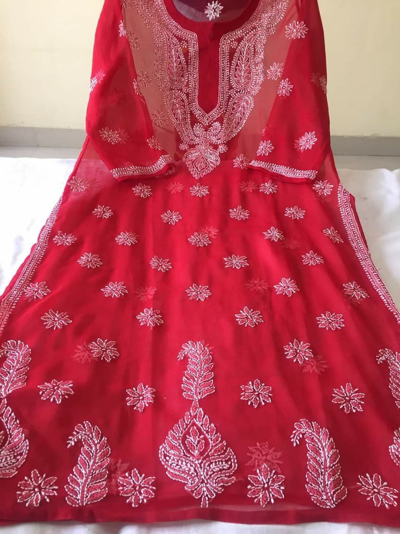 May include: A red sheer tunic with white embroidery. The embroidery features floral and paisley designs.