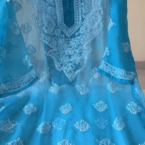May include: A turquoise blue sheer tunic with white embroidery. The embroidery features floral and paisley designs.