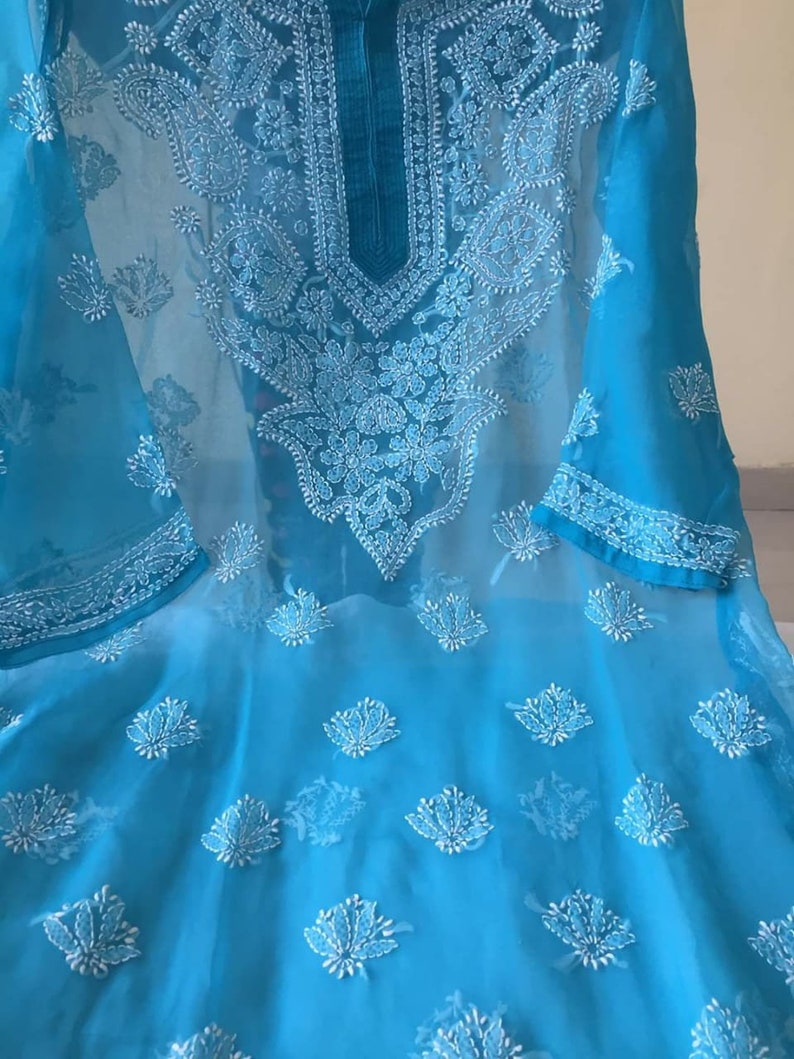 May include: A turquoise blue sheer tunic with white embroidery. The embroidery features floral and paisley designs.
