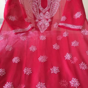 May include: A red sheer tunic with white embroidery. The embroidery features a floral pattern and a paisley design. The tunic has a round neckline and three-quarter sleeves.