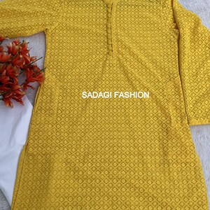 Pode incluir: Uma kurta amarela bordada com fecho de bot&atilde;o no pesco&ccedil;o. A kurta tem um padr&atilde;o floral e o texto "SADAGI FASHION" est&aacute; impresso na frente.