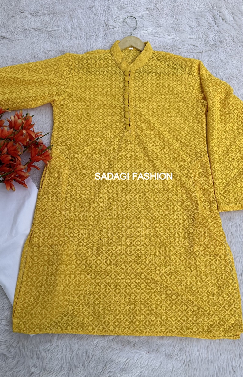 Pode incluir: Uma kurta amarela bordada com fecho de bot&atilde;o no pesco&ccedil;o. A kurta tem um padr&atilde;o floral e o texto "SADAGI FASHION" est&aacute; impresso na frente.