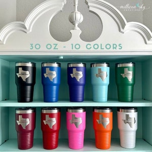 May include: Ten 30 oz stainless steel tumblers in various colors. Each tumbler features a Texas outline with the text "Save Texas" inside. The tumblers are arranged in two rows of five on a shelf.