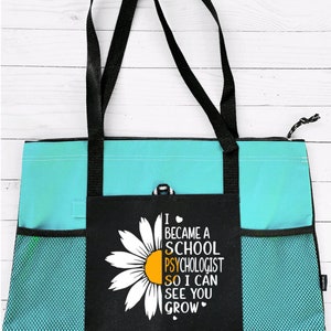 May include: A turquoise and black tote bag with a white daisy and the text "I became a school psychologist so I can see you grow".