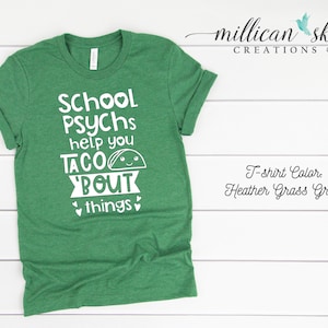 May include: Green t-shirt with white text that reads "School Psychs help you taco bout things" with a cartoon taco graphic. The t-shirt color is Heather Grass Green.