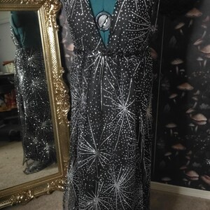 Peut inclure: Une robe maxi noire &agrave; col en V et un motif d'&eacute;toiles argent&eacute;es. La robe est faite d'un tissu transparent et a une silhouette fluide.