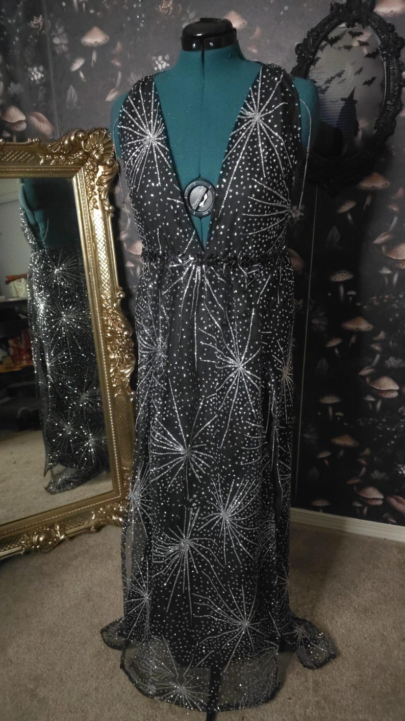 Peut inclure: Une robe maxi noire &agrave; col en V et un motif d'&eacute;toiles argent&eacute;es. La robe est faite d'un tissu transparent et a une silhouette fluide.