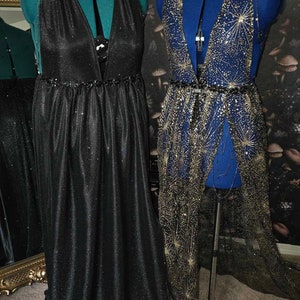 Peut inclure: Deux mannequins pr&eacute;sentent deux styles diff&eacute;rents de robes scintillantes. La robe de gauche est noire avec un col en V et une taille fronc&eacute;e. La robe de droite est une robe transparente bleu et or avec un col en V et une ceinture.