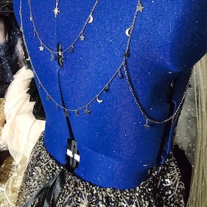 Peut inclure: Un corsage bleu avec un collier en cha&icirc;ne noire orn&eacute; d'&eacute;toiles et de croissants de lune. Le corsage est port&eacute; sur une jupe noire avec des paillettes dor&eacute;es et un ruban noir.