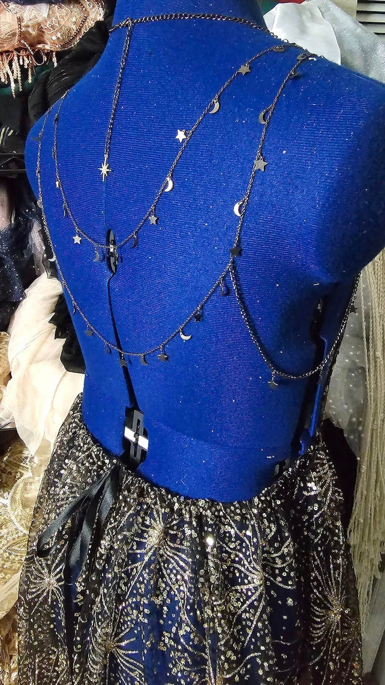Peut inclure: Un corsage bleu avec un collier en cha&icirc;ne noire orn&eacute; d'&eacute;toiles et de croissants de lune. Le corsage est port&eacute; sur une jupe noire avec des paillettes dor&eacute;es et un ruban noir.