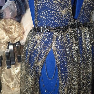 Peut inclure: Une robe en maille noire avec des &eacute;toiles dor&eacute;es scintillantes et une ceinture noire. La robe a un d&eacute;collet&eacute; en V profond et une longue jupe fluide.