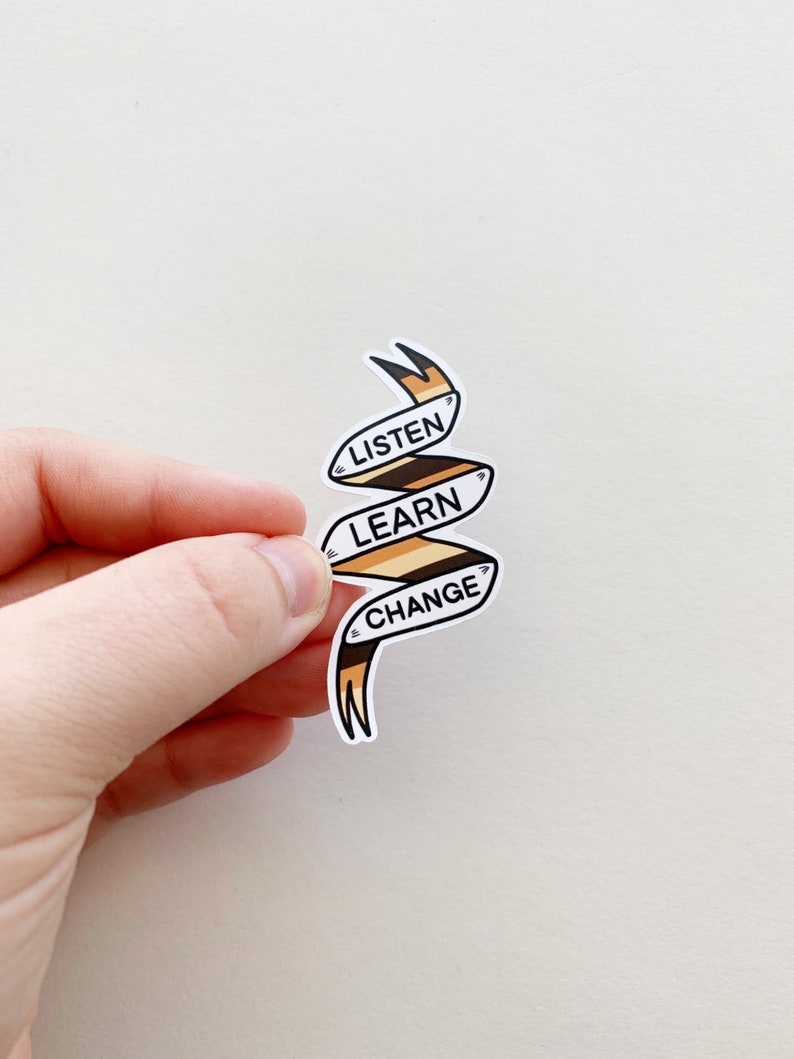 May include: A white sticker with a brown and orange ribbon design. The ribbon is curled and has the words "LISTEN", "LEARN", and "CHANGE" written on it.