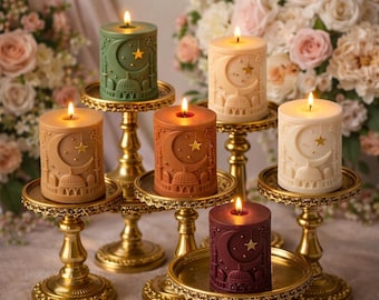 May include: A collection of lit, pillar-style candles in various colors, including green, tan, and burgundy. Each candle features a crescent moon, star, and mosque design. The candles are displayed on ornate, gold-colored stands.