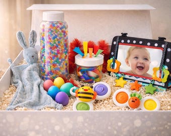 May include: A gift box containing baby toys: a plush bunny, a jar of colourful beads, and a framed photo of a smiling baby. Also included are colourful eggs and various sensory toys.