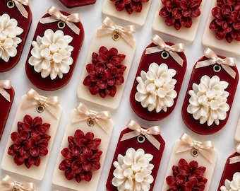 May include: An array of decorative gift tags with floral designs. The tags have either a cream rectangular base or a deep red tag, each with a 3D flower in cream or deep red. A gold ribbon bow is tied at the top of each tag, adding a touch of elegance.