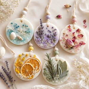 May include: Five round, white wax air fresheners with dried flowers and botanicals. Each has a string for hanging and wooden beads. The scents include lavender, rose petals, dried orange slices, and seashells.