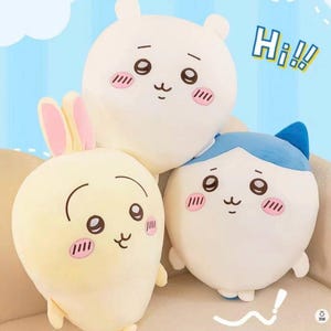 May include: Three plush toys in the shape of cartoon animals. The toys are a light yellow bunny with pink ears, a white bear, and a white cat with blue accents. Each has a cute face with blush marks and the word "Nice" and "Hi!!" in the background.