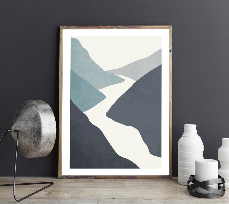 Op de afbeelding: Abstracte kunstprint met een witte rivier die door een blauw en grijs berglandschap slingert. De print is ingelijst in een licht houten lijst.