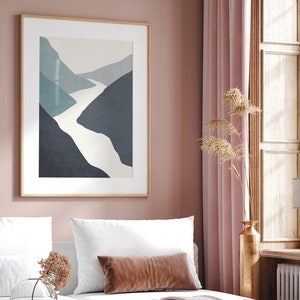 Op de afbeelding: Een ingelijste abstracte print van een witte rivier die door een blauw en grijs berglandschap slingert. De print hangt aan een roze muur in een slaapkamer.