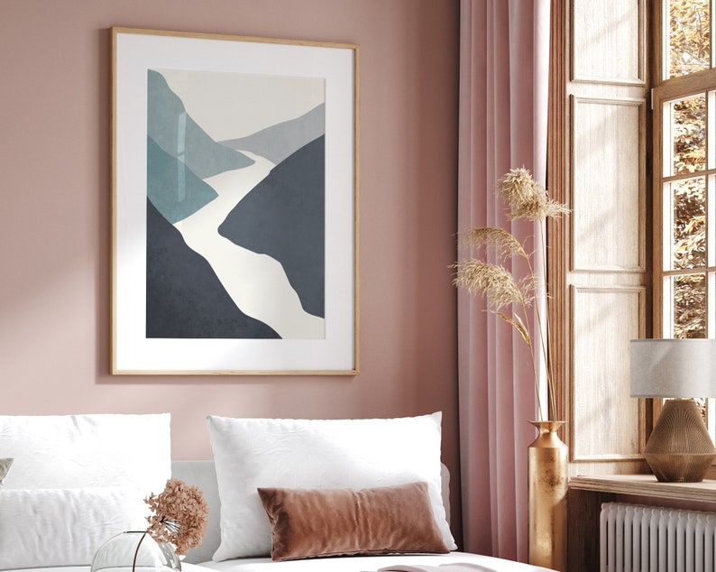 Op de afbeelding: Een ingelijste abstracte print van een witte rivier die door een blauw en grijs berglandschap slingert. De print hangt aan een roze muur in een slaapkamer.