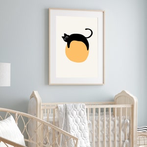Puede incluir: Un gato negro con ojos blancos est&aacute; tumbado sobre un c&iacute;rculo amarillo grande. La imagen est&aacute; enmarcada en un marco de madera claro y est&aacute; colgada en una pared azul claro.