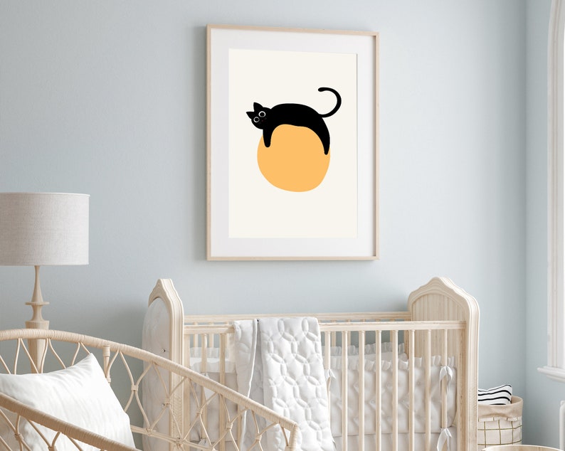 Puede incluir: Un gato negro con ojos blancos est&aacute; tumbado sobre un c&iacute;rculo amarillo grande. La imagen est&aacute; enmarcada en un marco de madera claro y est&aacute; colgada en una pared azul claro.