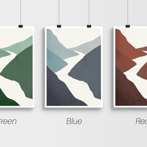 Op de afbeelding: Drie abstracte landschapsdrukken met een witte rivier die door groene, blauwe en rode bergen slingert. De prints zijn ingelijst met een witte rand en hangen aan een witte muur.