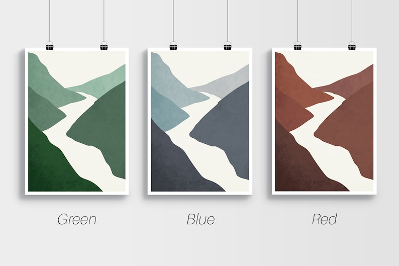 Op de afbeelding: Drie abstracte landschapsdrukken met een witte rivier die door groene, blauwe en rode bergen slingert. De prints zijn ingelijst met een witte rand en hangen aan een witte muur.