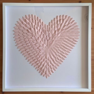 May include: A framed pink paper heart sculpture with a 3D effect. The heart is made of many small, overlapping paper pieces that create a layered look.