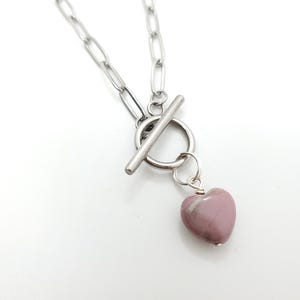 May include: A silver-toned chain necklace with a toggle clasp and a heart-shaped pendant. The pendant is a light pink stone with darker pink veining. The necklace is displayed against a white background.