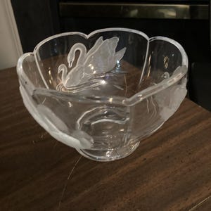 May include: A clear glass bowl with a scalloped rim and a frosted, etched design of a swan swimming on the interior surface. The bowl features a rounded base and a smooth, transparent finish, highlighting the detailed swan motif.