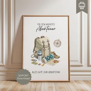May include: A framed print with a watercolour illustration of a backpack, compass, hiking boots, and map. The text "FÜR DEIN NÄCHSTES Abenteuer" and "ALLES GUTE ZUM GEBURTSTAG!" are displayed. A roll of 100 bills is also shown.