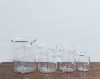 Juego de cuatro vasos de precipitados de vidrio recuperados para laboratorio de ciencias, con tamaños graduados.