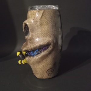 May include: A brown burlap tumbler with a black and white skull design and a blue and purple glitter design. The tumbler has a yellow and black bee design on the side.