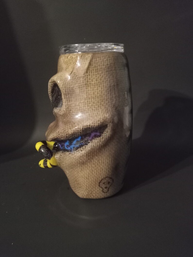 May include: A brown burlap tumbler with a black and white skull design and a blue and purple glitter design. The tumbler has a yellow and black bee design on the side.