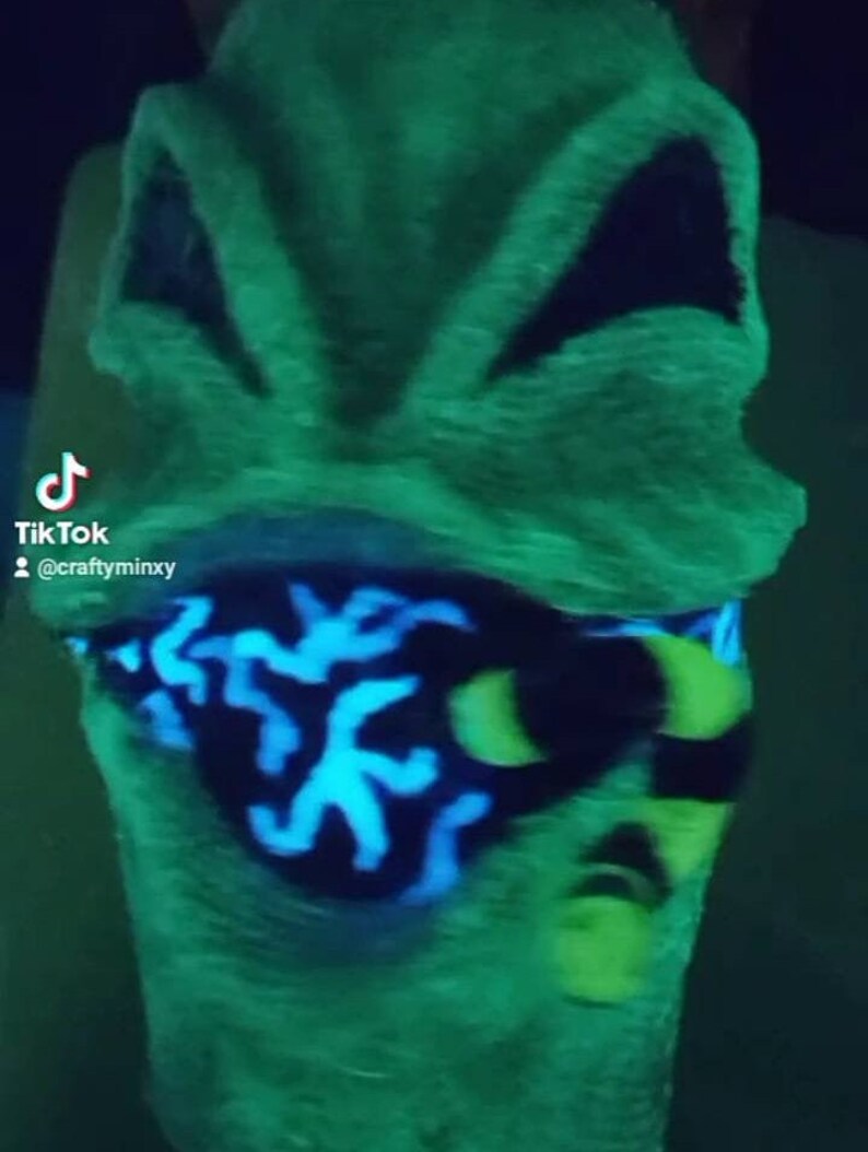 May include: A green glow-in-the-dark mask with black and blue details. The mask has a black eye mask with a blue and green pattern. The mask is made of a soft, fuzzy material.