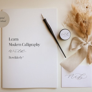 May include: A white booklet with the text "Learn Modern Calligraphy with Bewilderly" on the cover. A black calligraphy pen, a small jar of ink, and a piece of paper with the word "nib" written in calligraphy are also shown. The image has a rustic aesthetic with dried flowers and a beige ribbon.